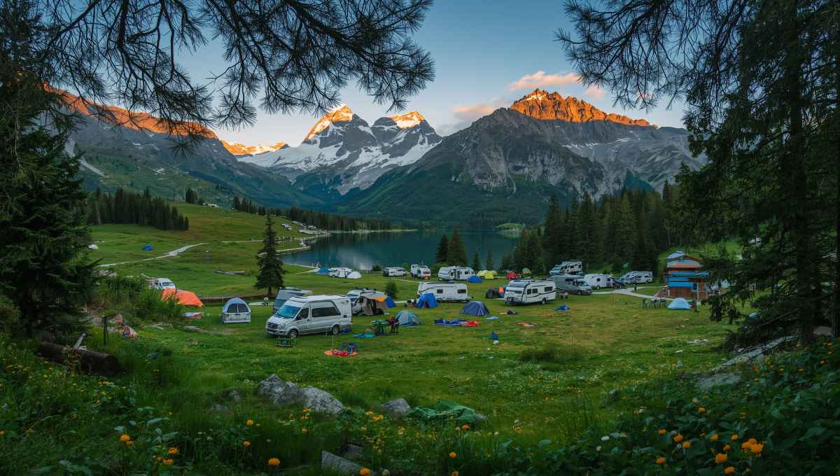 Camping en montagne dans les Alpes avec emplacements tentes et caravanes, panorama sur sommets enneigés et vallée verte